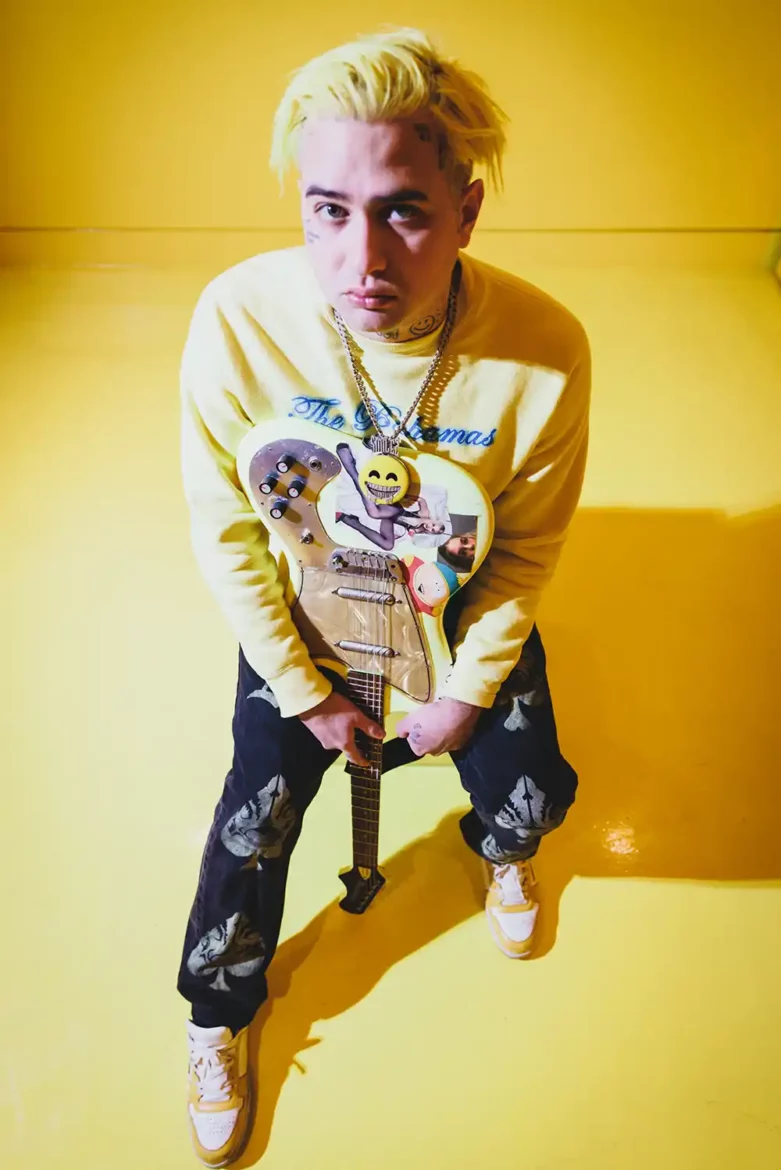 SMILEZ, the vibrant artist, posing with his guitar against a yellow backdrop during a photoshoot.