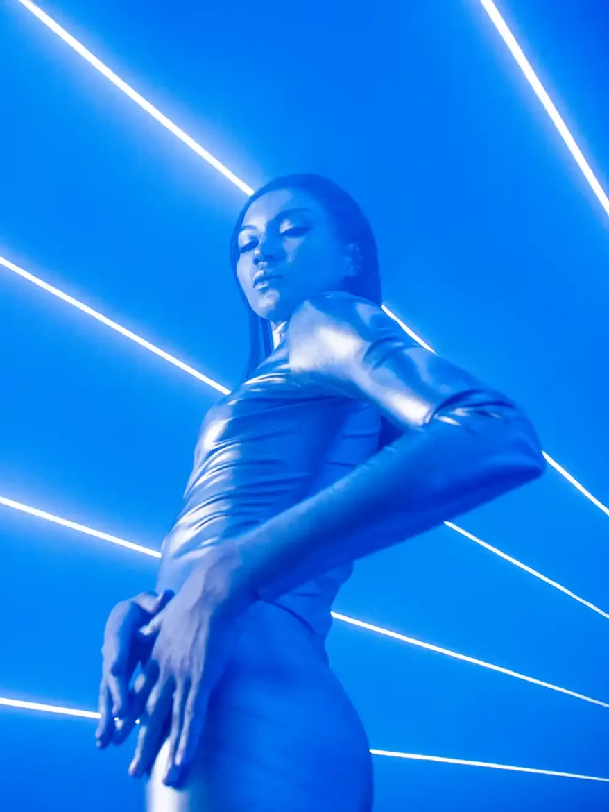 A female artist in a futuristic tight outfit with beams of blue lights in the background during a stunning photoshoot.