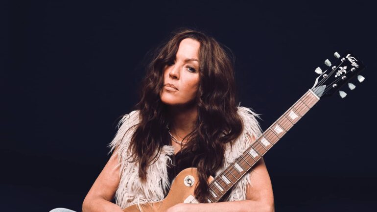 Mim Grey holding her guitar in a photoshoot.