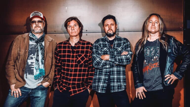 Four members of the hard rock band Jeet Kune Do pose for a group photo against a neutral background.