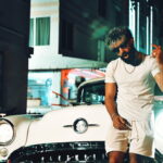 Artist Shubz stands by a classic car on a Miami street at night.