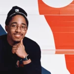 Smiling man in a black shirt, seated in front of an NBA logo backdrop.