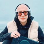 DJ Remo holding a MIDI controller on a beach, symbolizing his return to music production.