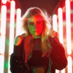 DJ Oskana stands amid vibrant neon lights, embodying the lively spirit of her song 'Extasy'.