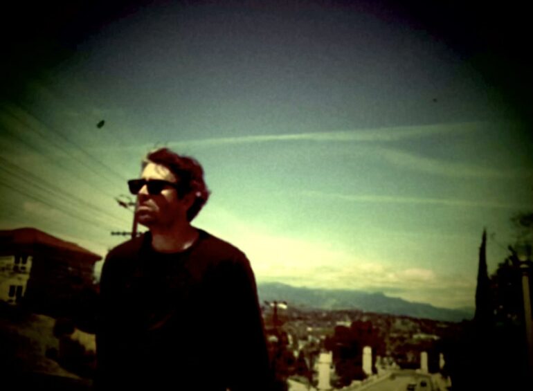 Man in sunglasses with a contemplative expression overlooking a cityscape.