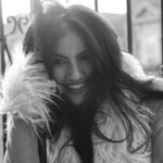 Adeline V. Lopez smiling and leaning against a balcony railing in a fur-lined coat.