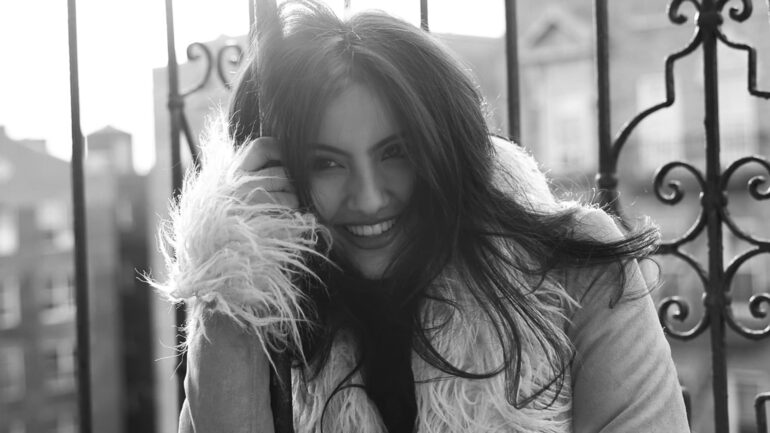 Adeline V. Lopez smiling and leaning against a balcony railing in a fur-lined coat.