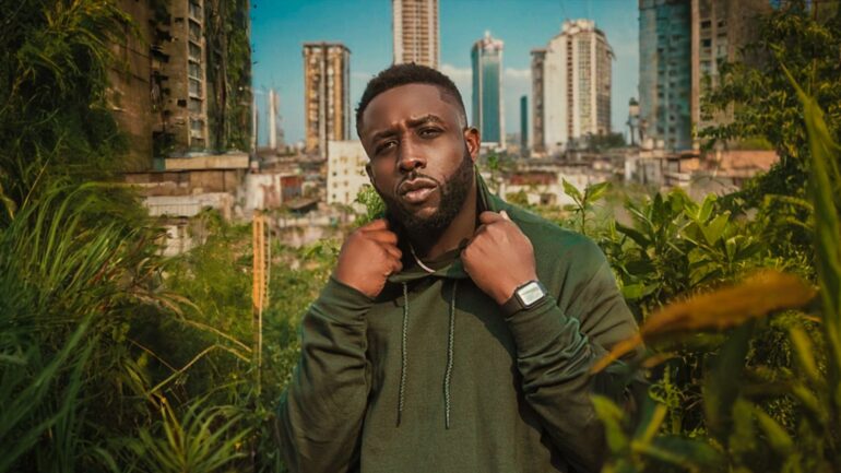 Michael O. stands in an urban jungle with high-rises in the background, promoting his new song 'Japa Remix.'