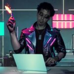 Mike Costanzo, also known as Electro Dream Magma, in a futuristic studio setting, wearing a neon-lit leather jacket and holding a flame torch.