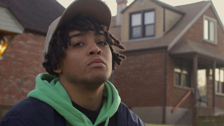 Che Sanchez performing his new single "Taken From Me" with emotional intensity in front of a house.