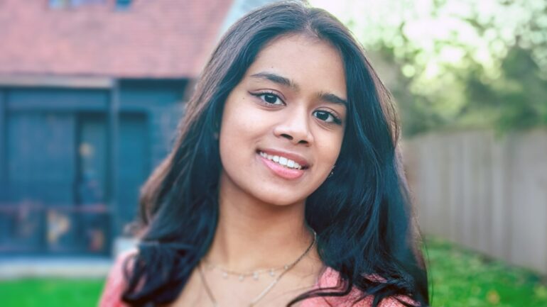 Diya Shanmugaraj smiling outdoors with a blurred background.