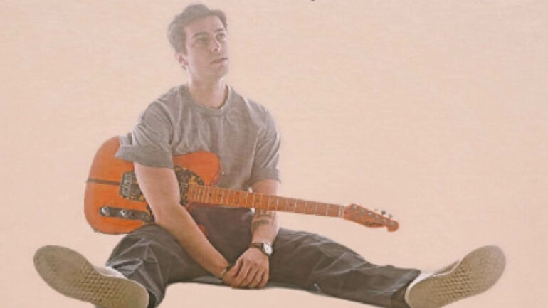 Evan Kreutz sitting with a guitar, promoting his new single "All You," showcasing a relaxed and introspective pose that complements the song's intimate theme.