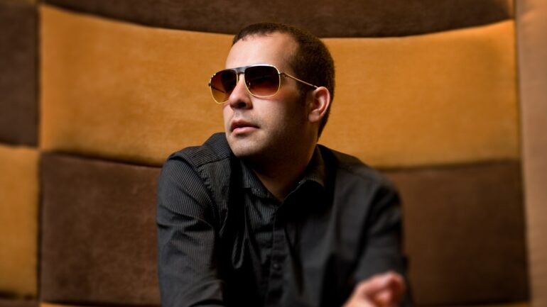 Joe Bermudez, seated in a stylish environment, wearing sunglasses and casual attire, promotes his latest track "Stop" released on 617 Records in 2024.