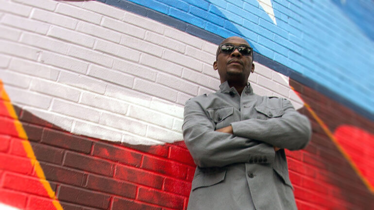 Poppastep posing against a colorful mural, wearing sunglasses and a grey jacket, promoting his new single ‘Fall Off’.