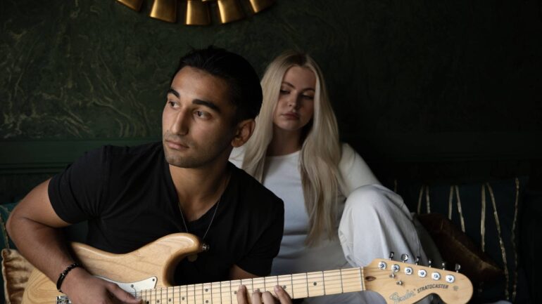 AJ Chaney playing guitar with a woman sitting behind him, reflecting the emotional tone of his debut single "Fading."