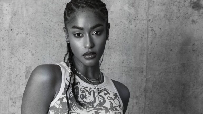 Ava Symone posing against a concrete wall in a stylish outfit, reflecting her unique music style.