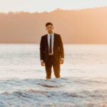 Josh Hearmon standing in the ocean in a suit at sunset, promoting his new single "Over Again."