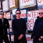 The band MAWK3 standing in front of a wall of televisions with provocative messages. Members Steve Giles, Jason Sweeny, and Dan Nelles are pictured.