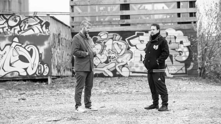 Bogart. (Marin and Jayztylez) stand in front of graffiti-covered walls, highlighting their collaboration on the new hip hop track "Dark Star Demoralizer."