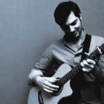 Emilio Lanza playing acoustic guitar in a black and white image, highlighting his emotional connection to music.