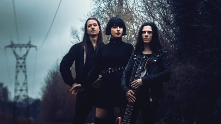 Band members of Oïkoumen standing in a forest under power lines, conveying a dark, atmospheric look.