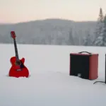 Red guitar and speaker with a Santa hat labeled "JK" on snow, set against a snowy forest background, promoting "The Cowbell Song (Merry Christmas).