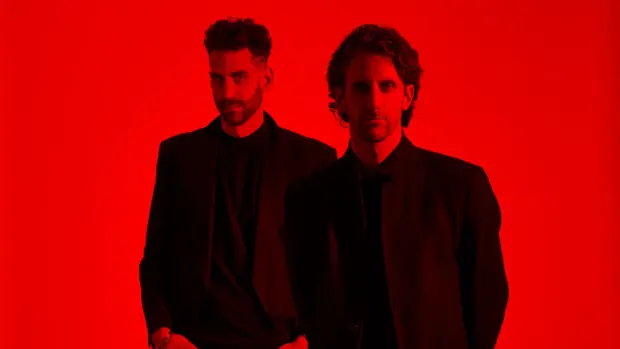 The Listros band members standing against a bold red background, wearing dark outfits, highlighting their intense and edgy aesthetic.